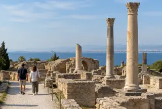 Vestiges des thermes d’Antonin à Carthage avec deux visiteurs et le golfe de Tunis en arrière-plan.