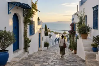 Ruelle blanche et bleue de Sidi Bou Saïd descendant vers le golfe de Tunis, avec une personne marchant au milieu des façades traditionnelles.